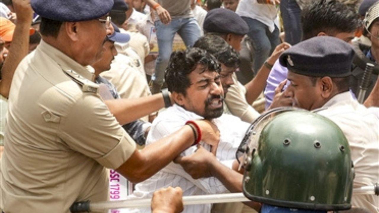 Male protester being pushed and restrained by police personnel during a protest march in Patna. Several police officers are seen surrounding and holding the man.